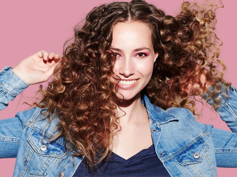 woman with curly hair type holding hair and smiling. what's my hair type?