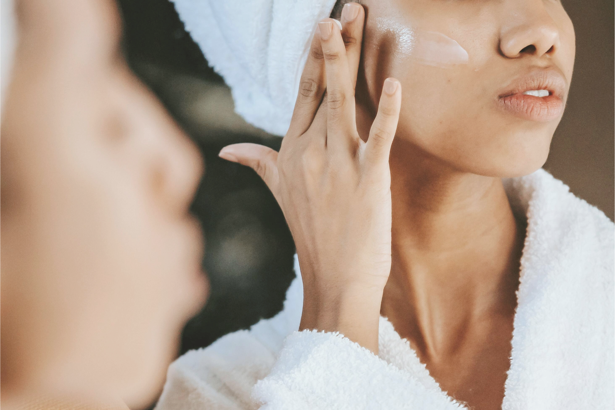 Chemical vs. physical exfoliation - a woman looking in the mirror while applying a chemical exfoliant